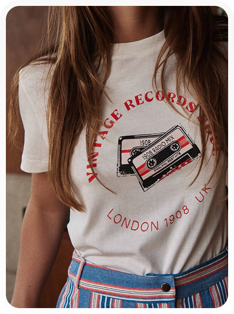 Woman wearing a white T-shirt with a red and black cassette tape design and text 'VINTAGE RECORDS', '1908 RADIO MIX', and 'LONDON 1908 UK', paired with blue striped pants.